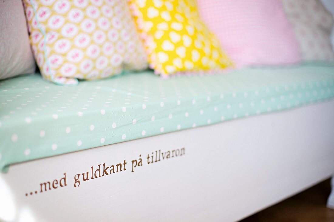 Bench with painted motto and pastel, patterned scatter cushions on polka-dot seat cushion