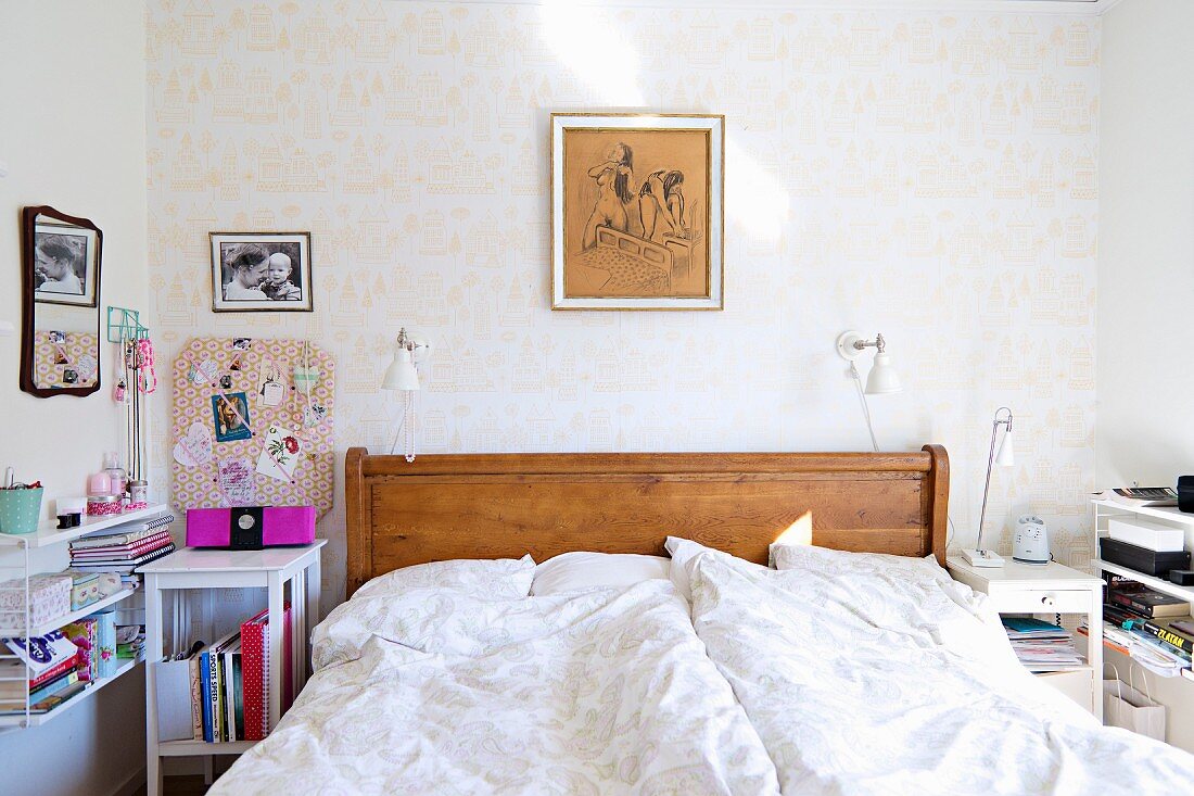 Double bed with wooden headboard and white bed linen next to white-painted bedside table and String shelves