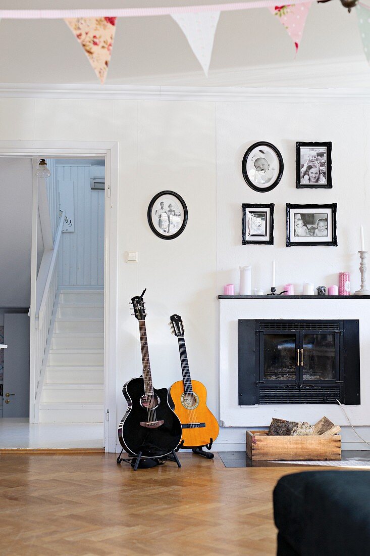 Guitars next to open fireplace below framed family photos in rustic living room
