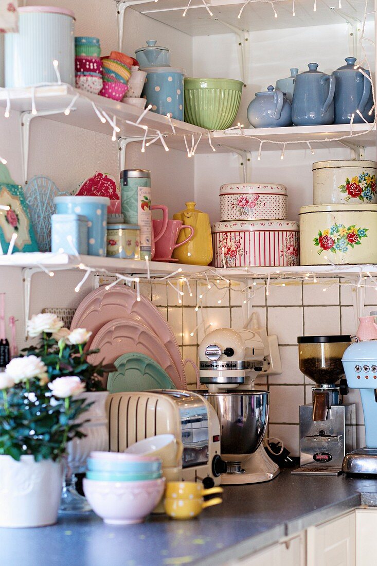 Pastellfarbenes Retro Geschirr auf Regal, dekoriert mit Lichterkette, über Küchenzeile