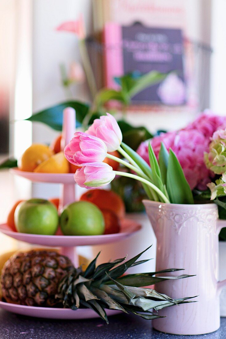 Tulpen in rosa Keramikkrug neben Etagere mit Früchten