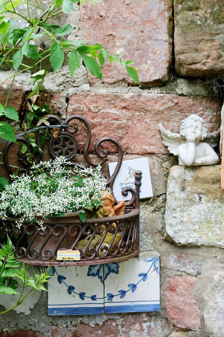 Rustikale Backsteinmauer mit Dekoengel und Metallbehälter mit blühendem Blumentopf