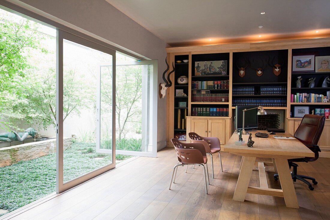Solid wooden desk and office chair in front of bookcase and opposite glass wall
