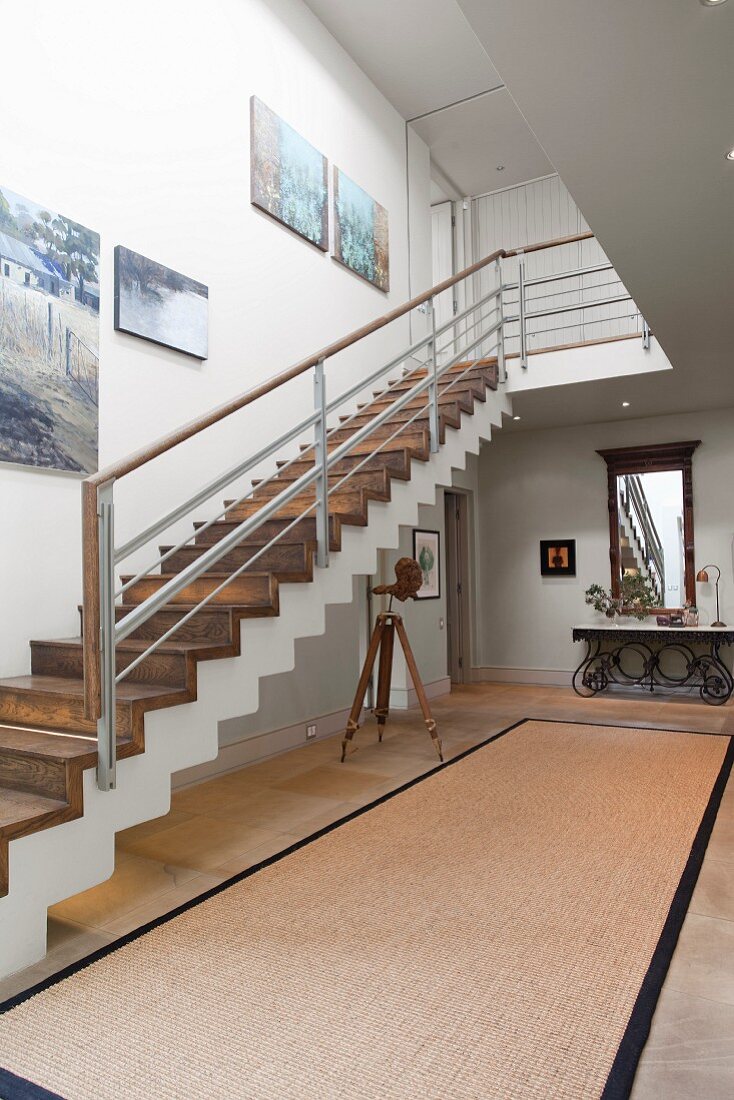 Staircase with wooden treads in bright, spacious hallway with modern bust on tripod