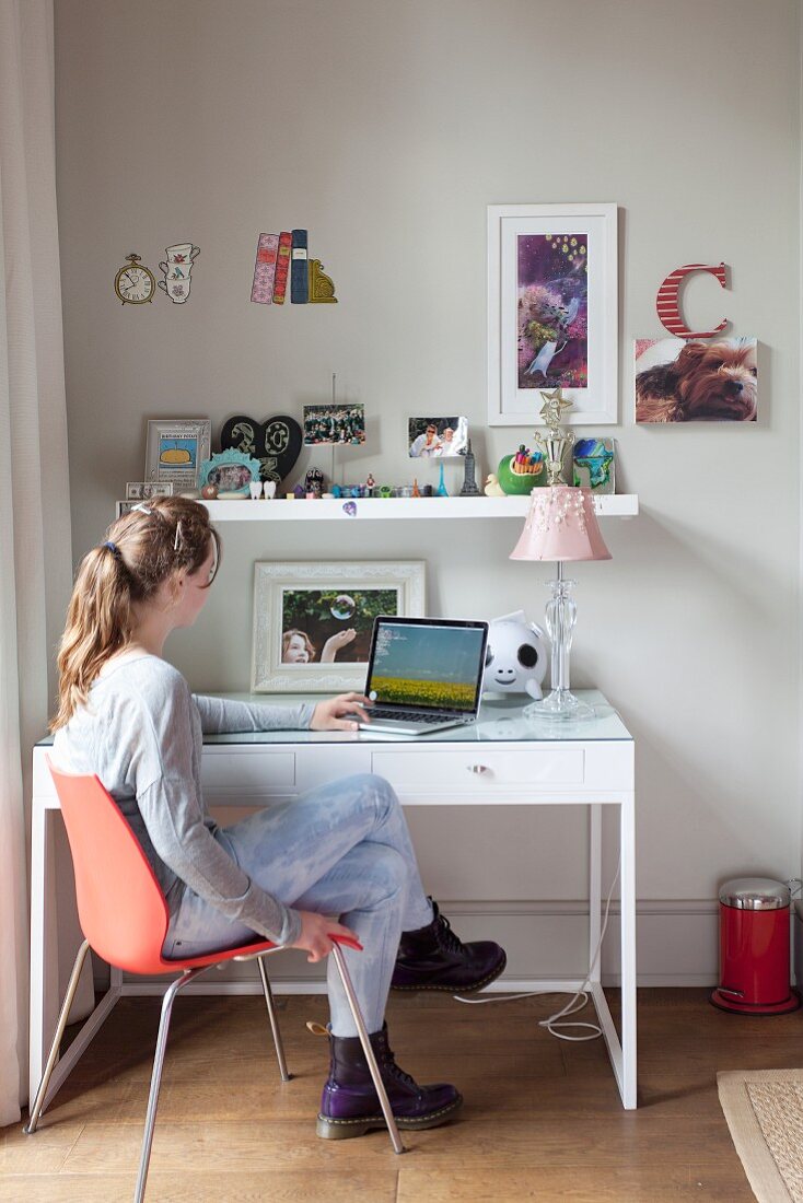 Mädchen mit Laptop am Schreibtisch, darüber Wandboard