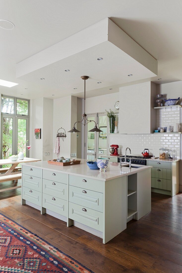White, open-plan, country-house kitchen with oak floor and island counter