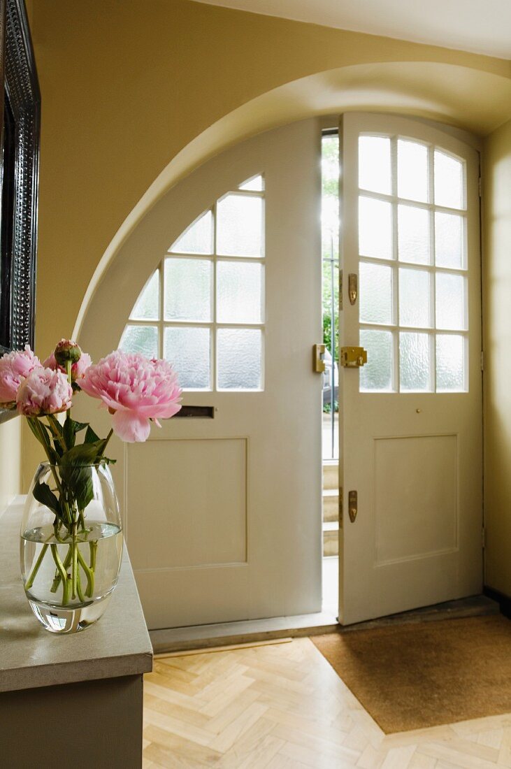 Rundbogen Haustür mit Sprossenverglasung in Vorraum eines Hauses, im Vordergrund Blumenstrauss auf Wandkonsole