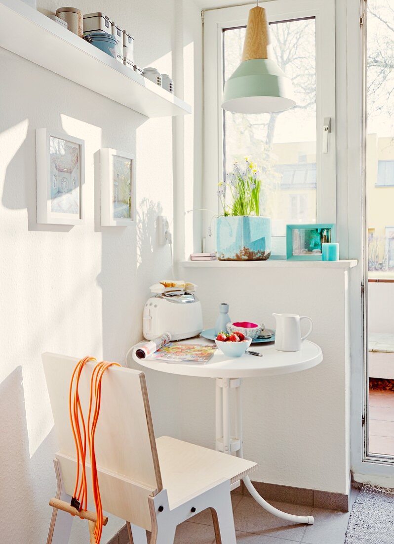 Moderner Brettstuhl am runden Frühstückstisch mit Blick auf den Balkon; Designerleuchte mit Holzfassung