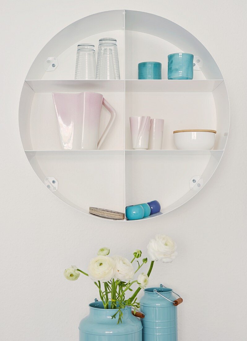 Circular shelving holding china and glasses; white ranunculus in blue enamel churns