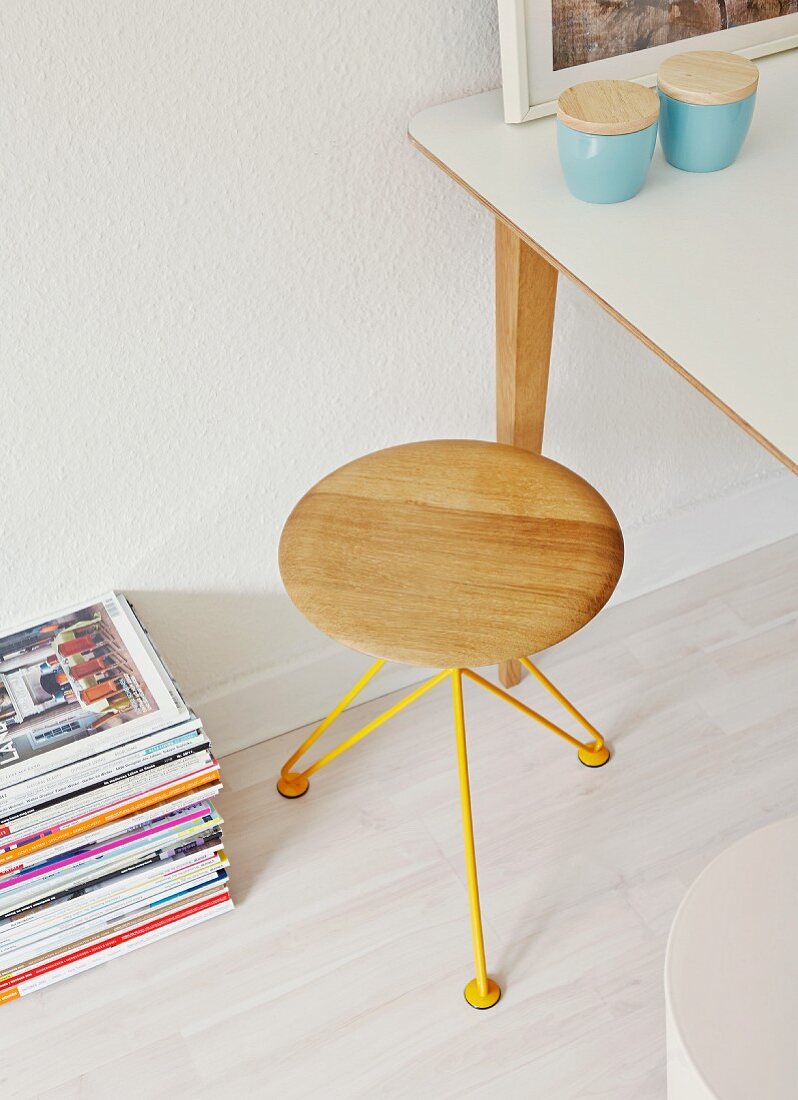 Designerhocker mit gelbem Drahtgestell, Porzellandosen mit Holzdeckel auf Tisch und Zeitschriftenstapel am Boden
