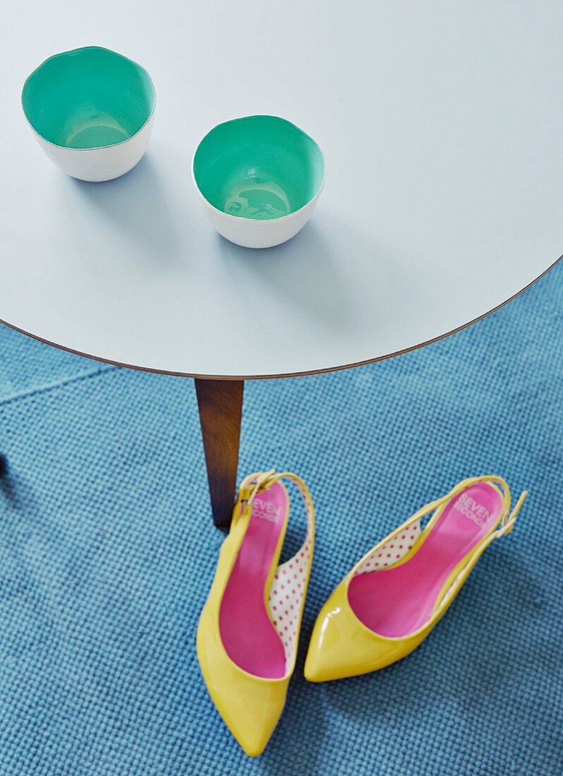 Tea bowls with mint-green interiors on delicate side table and bright yellow high heels on rug