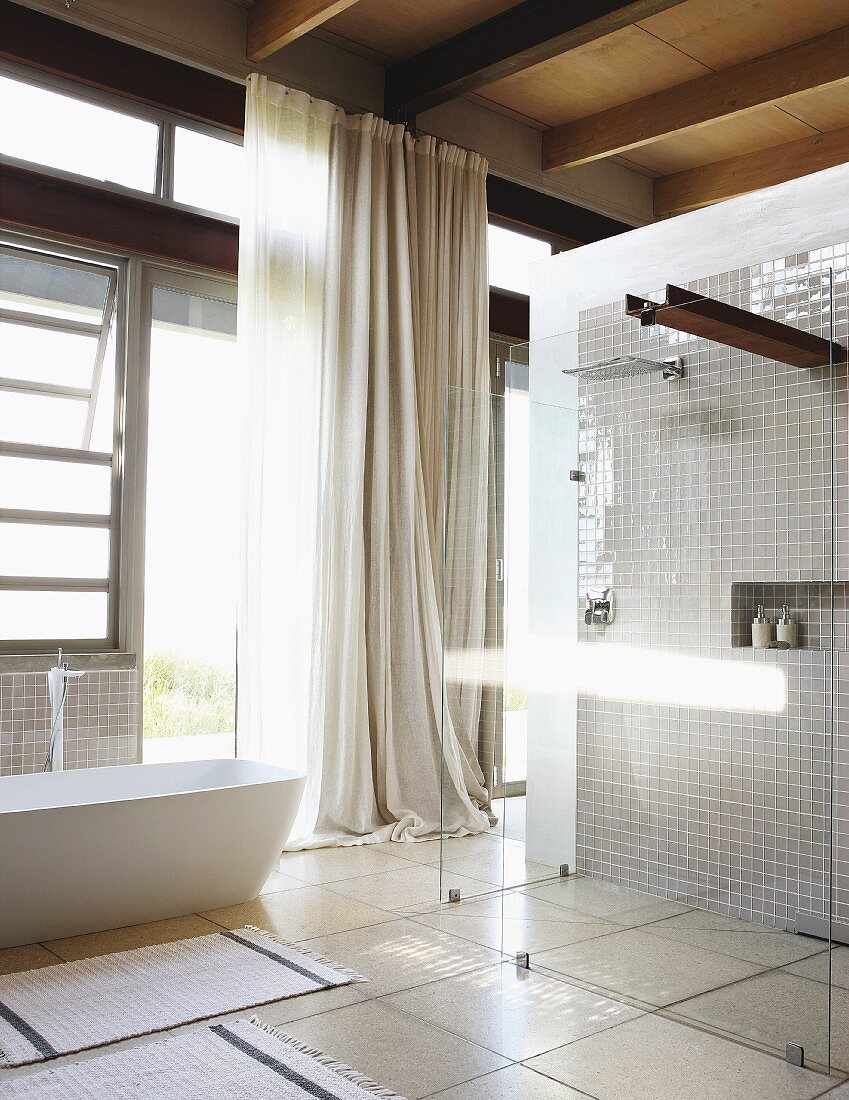 Light-flooded bathroom with walk-in designer shower and free-standing bathtub against steel and glass facade