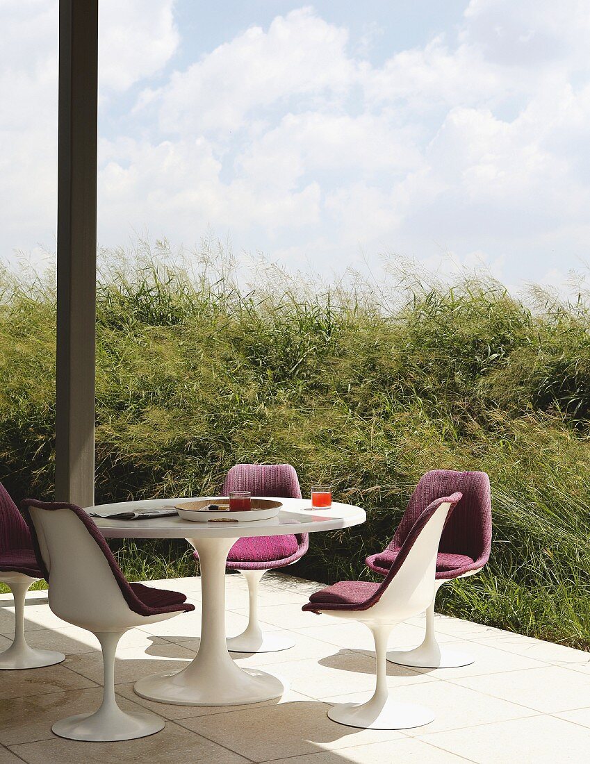 Tulpenstühle und Tisch auf sonniger Terrasse, geschützt durch umgebende Natur mit begrüntem Hügel