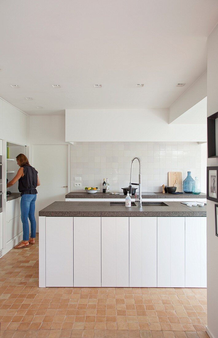 White fitted kitchen with dark worksurfaces, white tiles and terracotta tiled floor