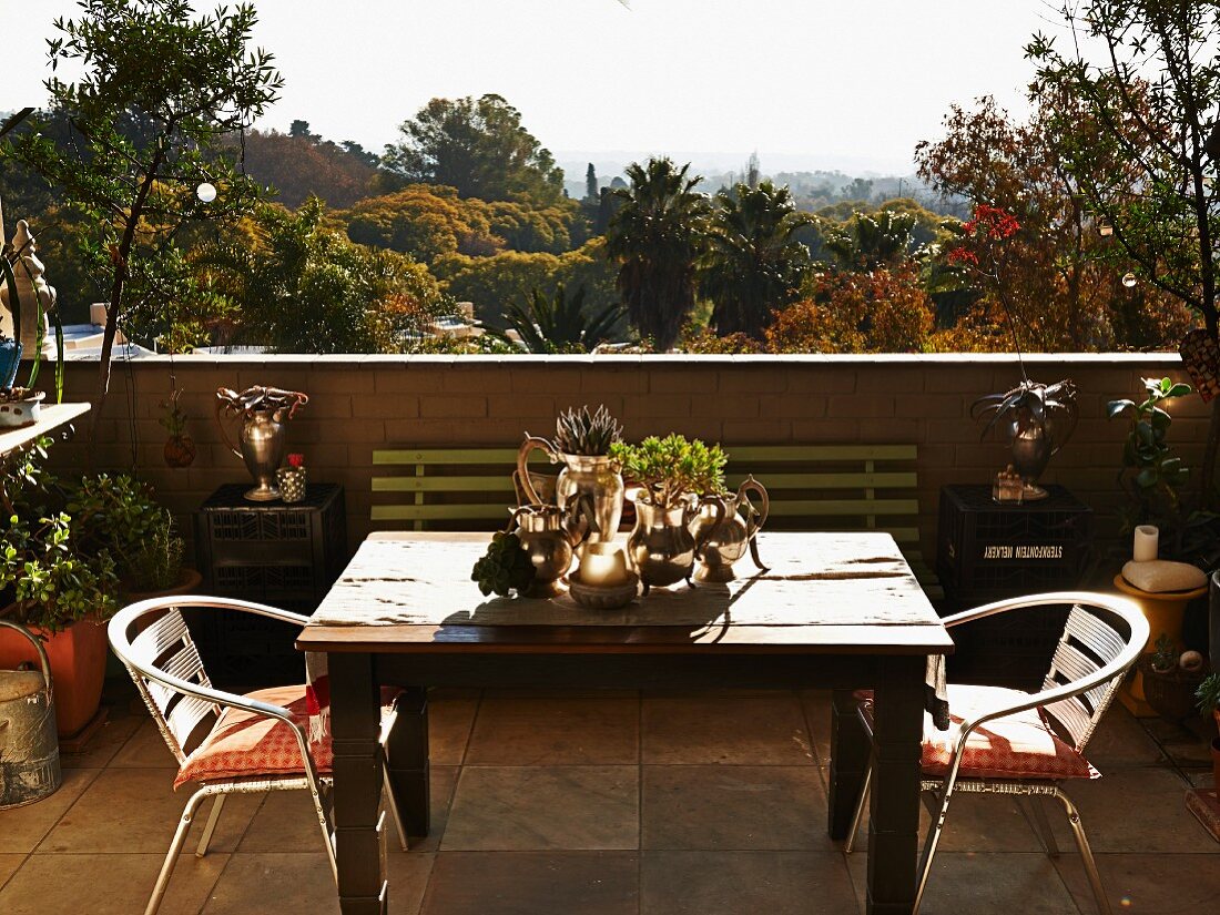 Wooden table and metal chairs on terrace with view across tropical landscape