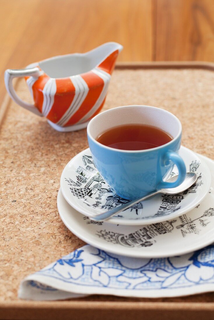 Eine Tasse Tee mit Untertasse und Retro Milchkännchen auf Korktablett