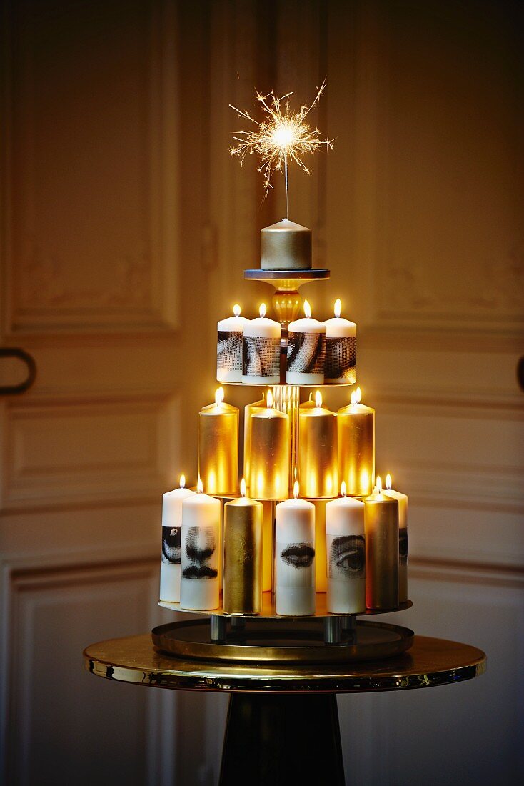 Moderner Christbaum aus pyramidenförmig arrangierten weissen und goldenen Kerzen mit Wunderkerze auf der Spitze