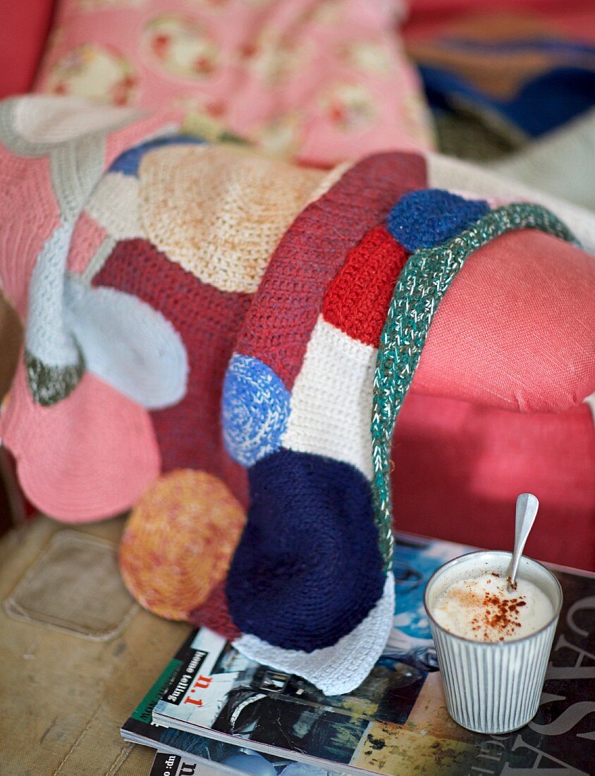 Cocoa with milk foam in a mug in front of a sofa with a knitted blanket
