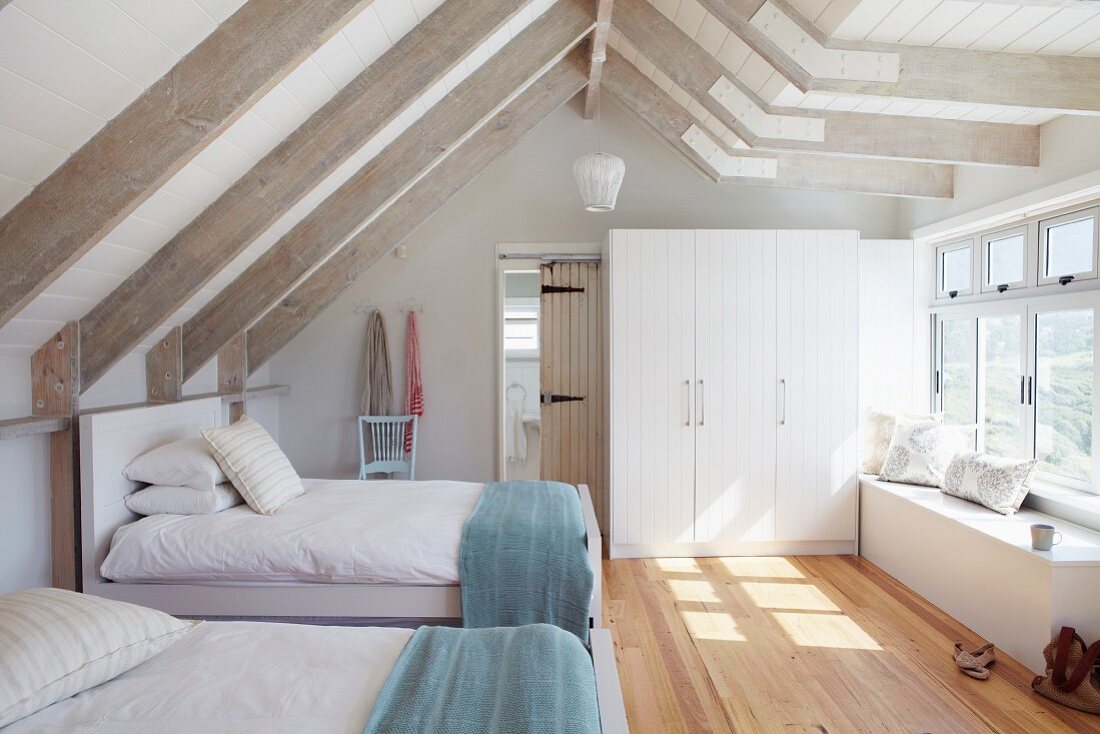 Guest bedroom with twin beds in bright attic room with white-painted wooden beams and parquet floor