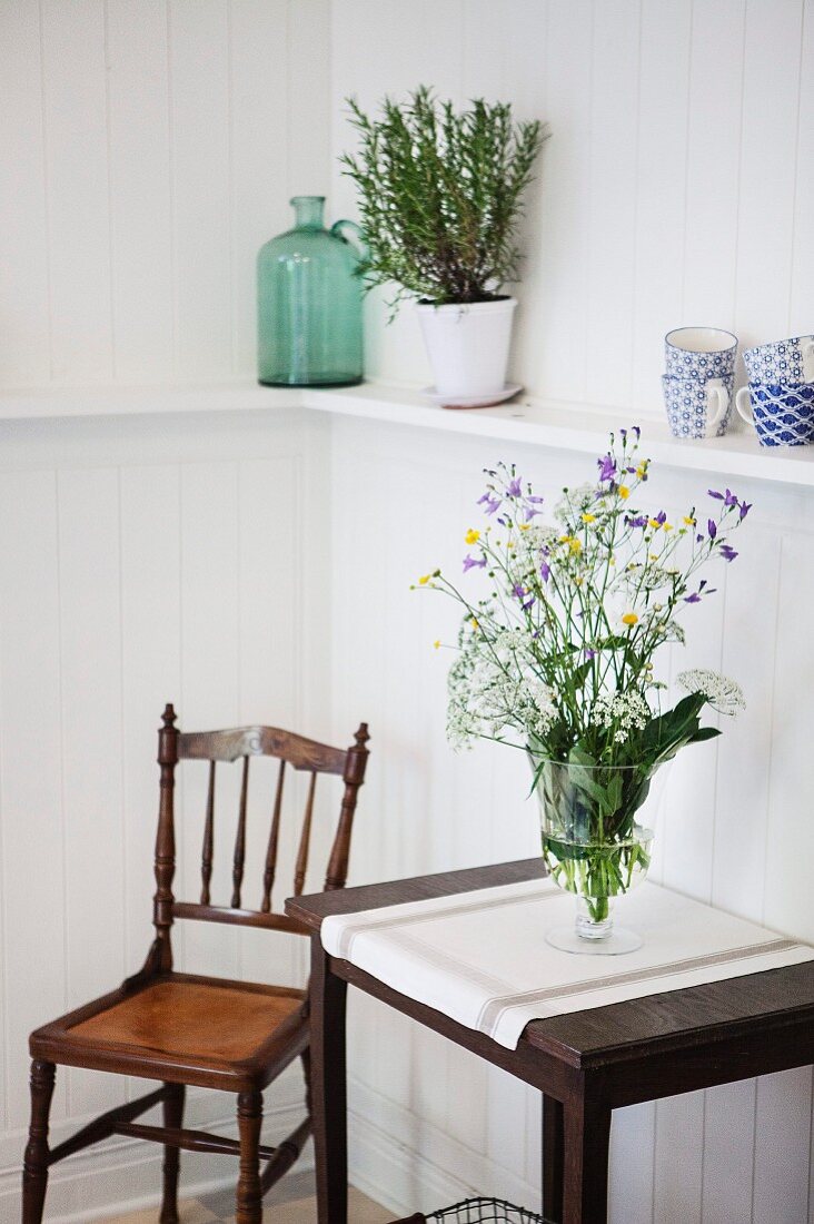 Glass vase of wildflowers on console table next to antique wooden chair