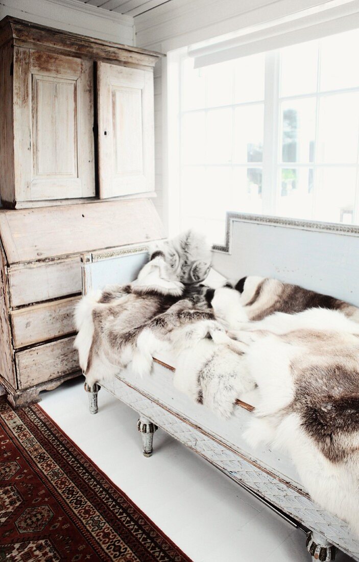 Animal-skin rugs on antique bench below window and antique wooden dresser