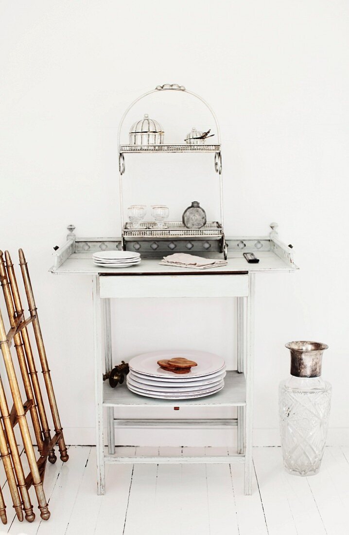 Zierlicher Beistelltisch aus weiss lackiertem Holz, mit Geschirr und Deko-Regal mit Silberdöschen