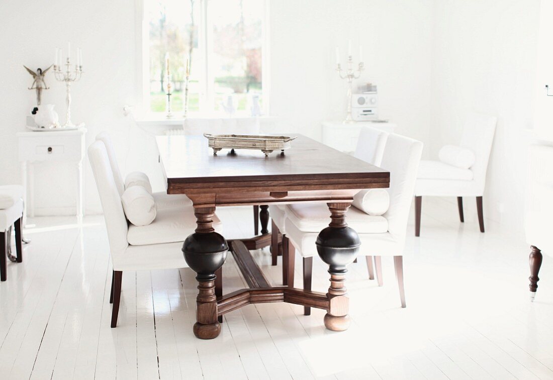 Dunkler Massivholztisch mit gedrechselten Beinen und elegante Polsterstühle in Weiß, auf rustikalem Dielenboden