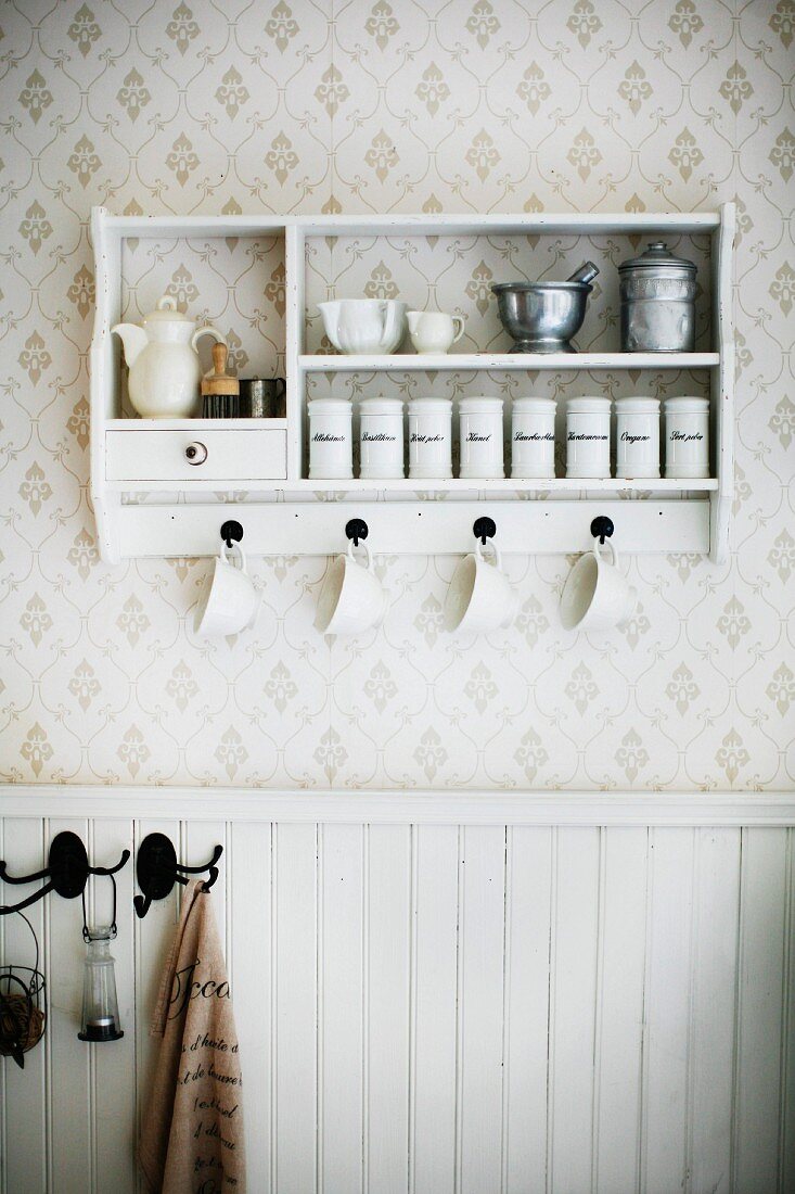 Weisses Gewürzregal mit Aufbewahrungsbehältern und Küchenutensilien an tapezierter Wand aufgehängt