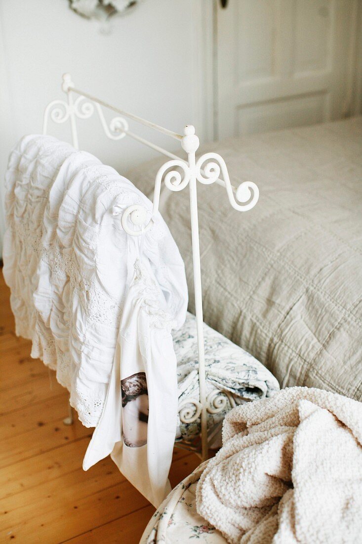 Ornate, white-painted, metal valet stand at foot of bed