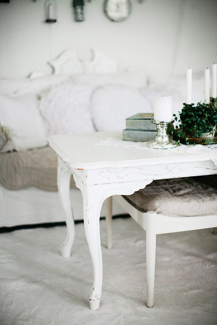 Candles on white-painted coffee table with curved legs and upholstered footstool in front of sofa