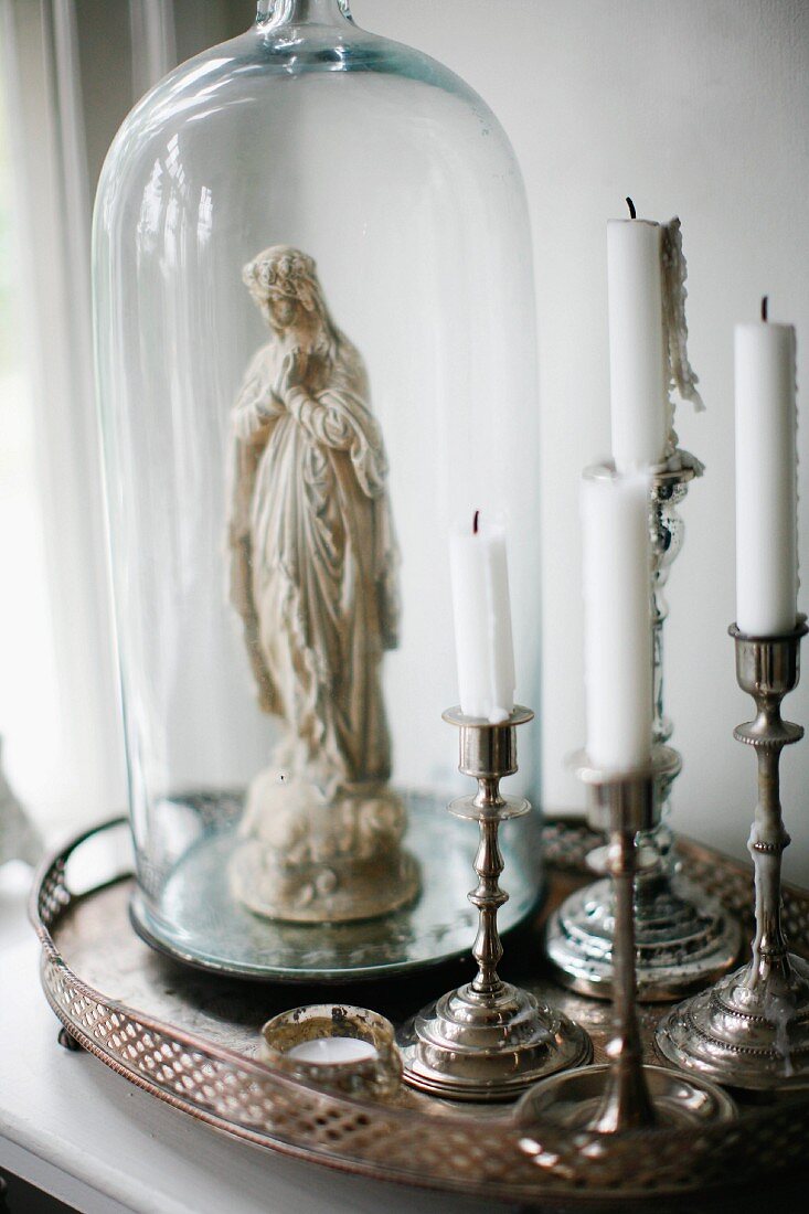 Silber Kerzenständer neben Madonnenfigur unter Glashaube, auf Silber Tablett