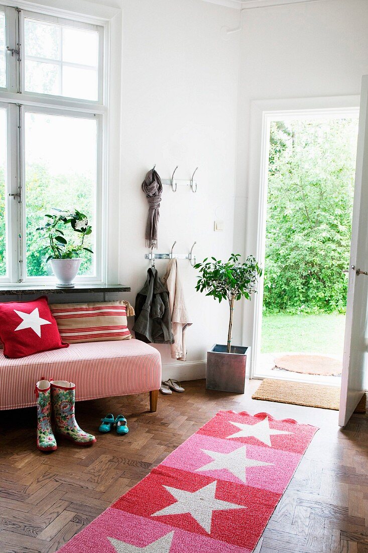 Rot und rosa gestreifter Teppichläufer mit Sternenmotiv in gemütlichem Wohnraum, offene Haustür und Blick in sommerlichen Garten