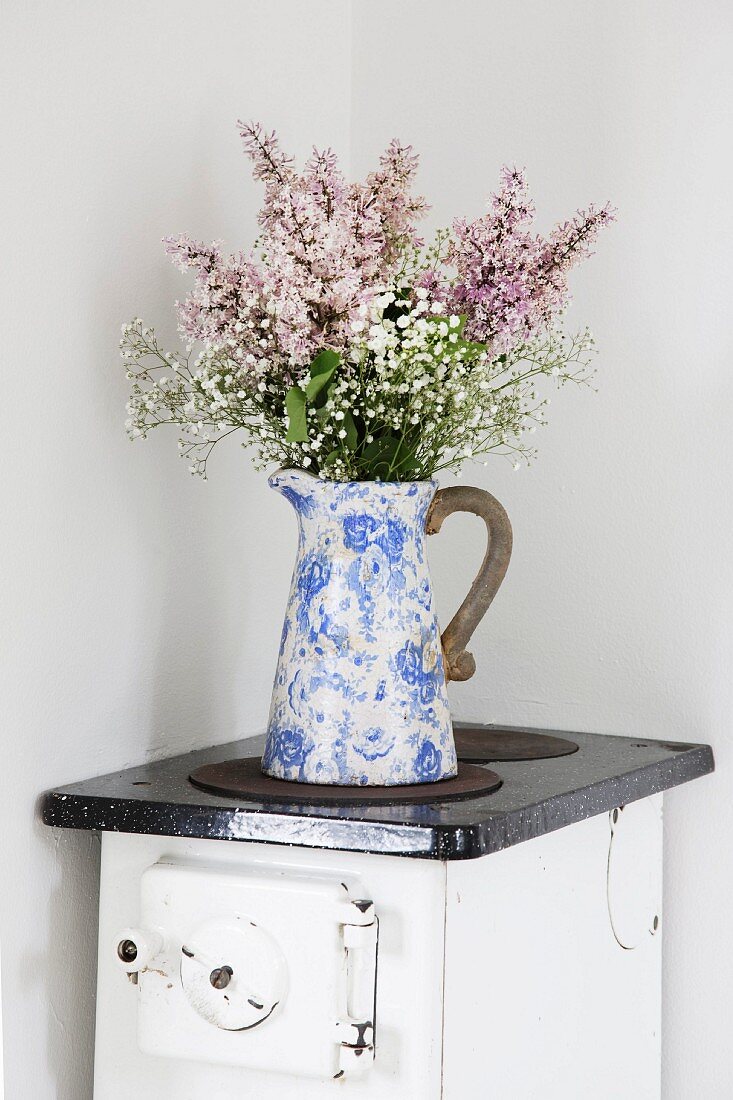 Vintage Krug mit Blumenstrauss auf altem Küchenofen in der Ecke