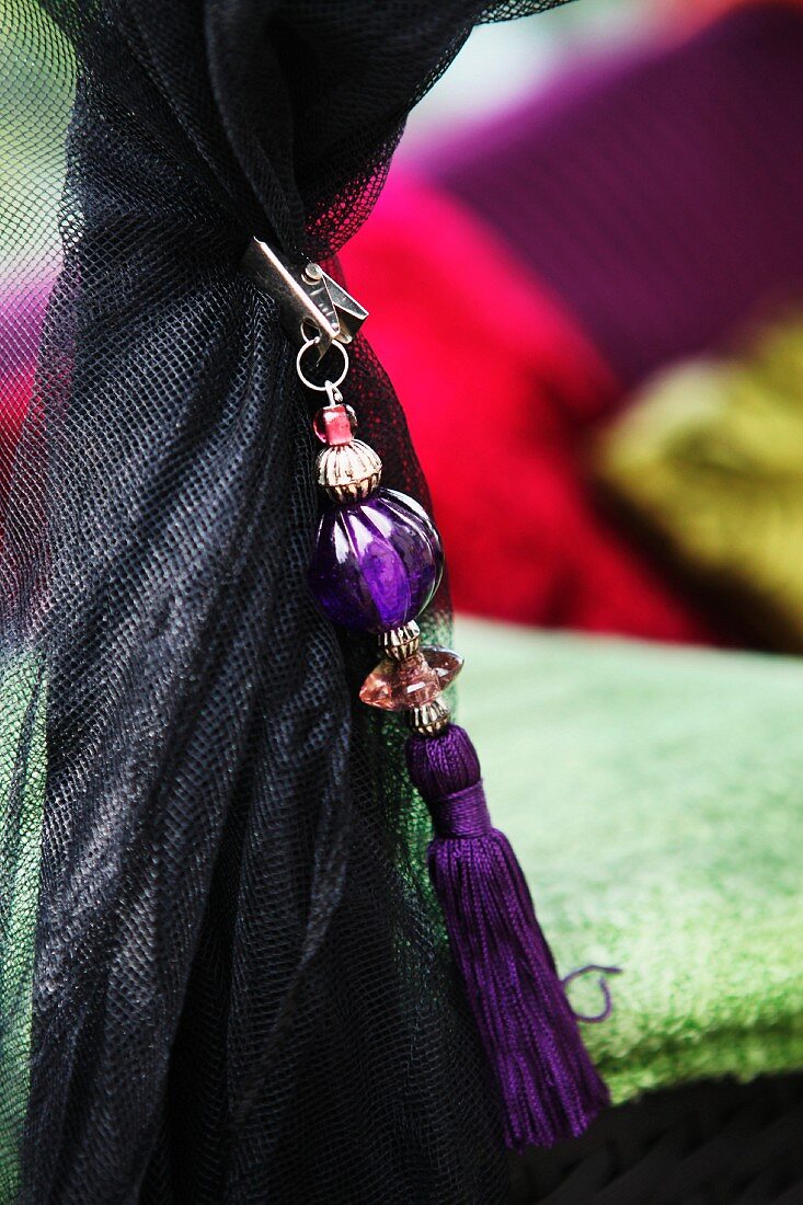 Orientalischer violettfarbener Anhänger mit aufgefädelten Glasperlen und Quaste an schwarzes Moskitonetz geklemmt
