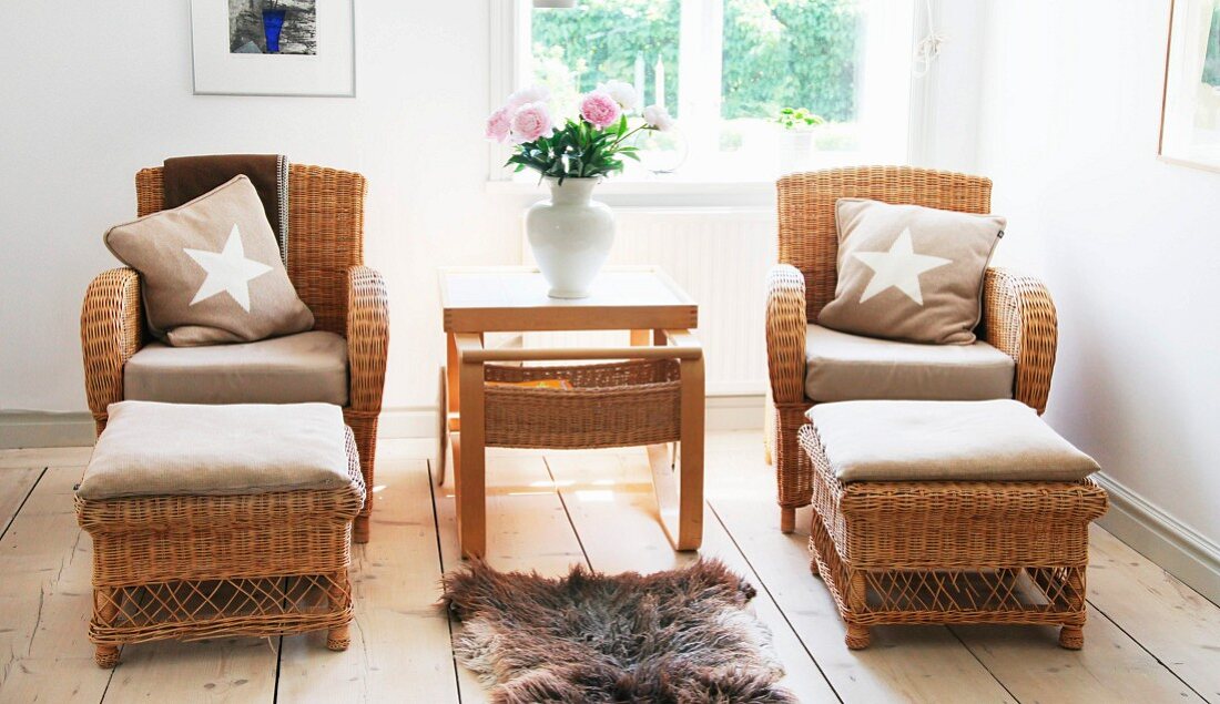 Side table flanked by wicker armchairs and foot stools below window