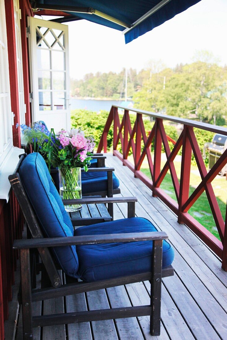 Dunkle Gartenmöbel mit blauen Polstern auf Holzveranda vor schwedischem Wohnhaus