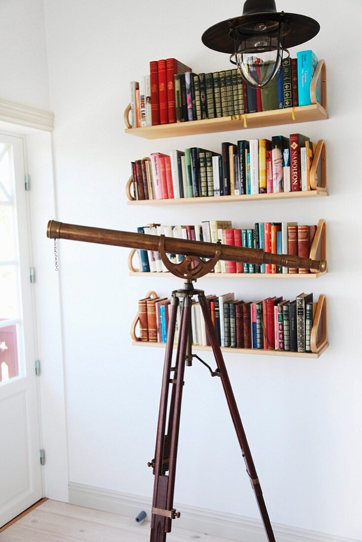 Retro pendant lamp above antique telescope in front of books on wall-mounted shelves
