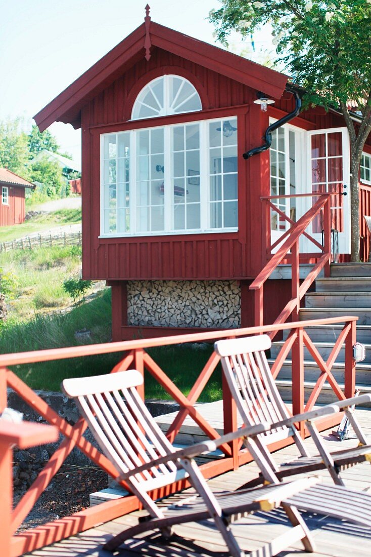 Deckchairs auf Holzsteg mit rotem Geländer unterhalb eines schwedischen Holzhauses am Meer