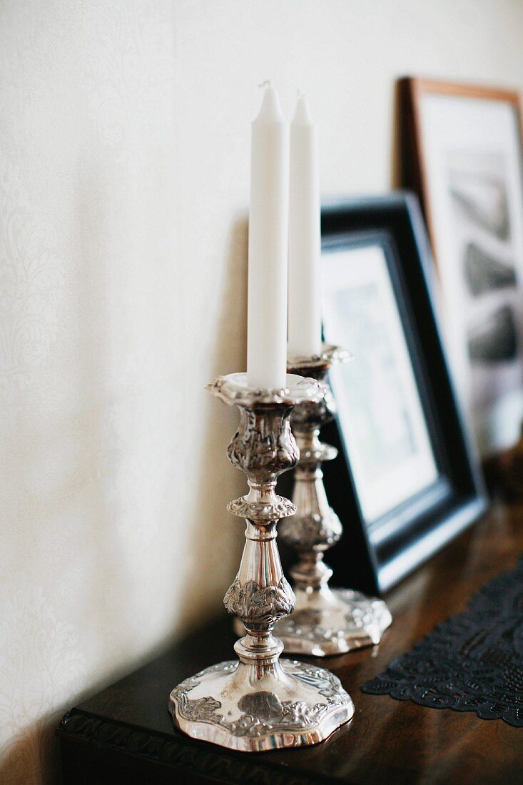 Silberne Kerzenständer mit weissen Kerzen auf Kommode