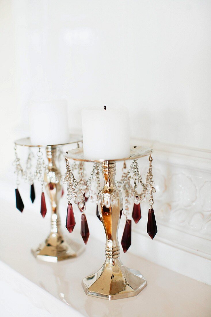 Candlesticks with colourful glass pendants and white pillar candles on mantelpiece