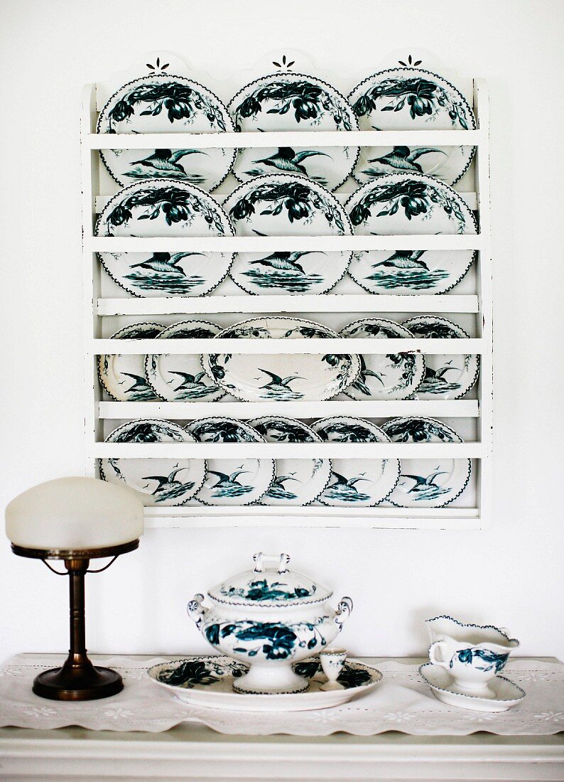 Wandregal mit bemalten Deko Tellern, davor antike Tischleuchte und Porzellangeschirr auf Ablage