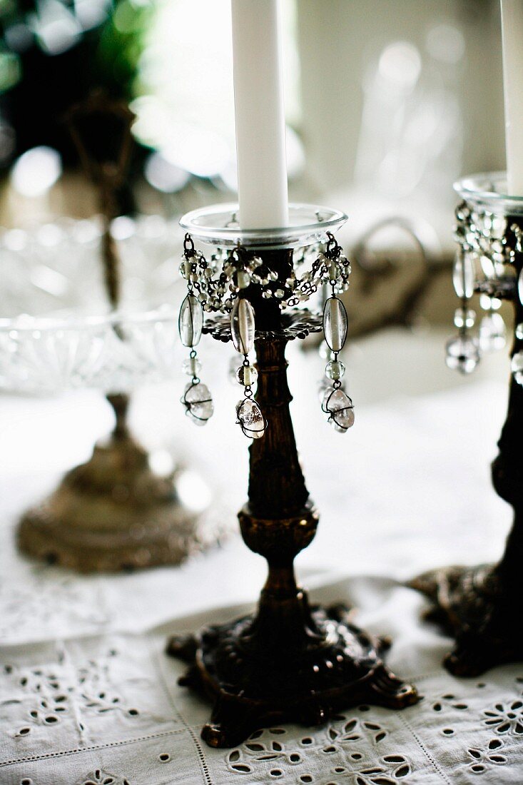Antiker Kerzenständer mit Perlenschmuck und weisser Kerze auf Tischdecke