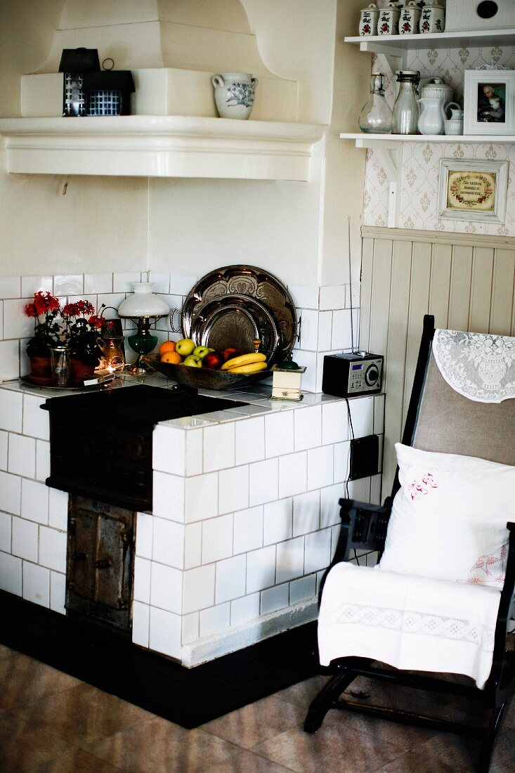 Alter Küchenstuhl mit Kissen neben gemauertem Küchenherd mit weissen Fliesen in Zimmerecke