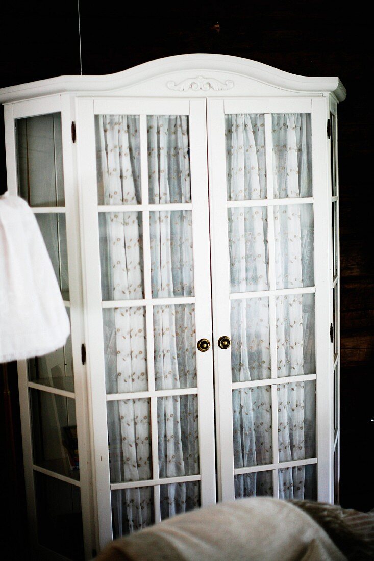 Weiß lackierter Vitrinenschrank, hinter Tür gemusterter Stoff