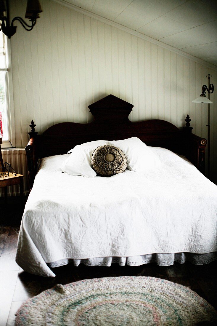 Französisches Bett mit schwarzem, geschnitztem Kopfteil und weiße Tagesdecke im Elternschlafzimmer unter dem Dach