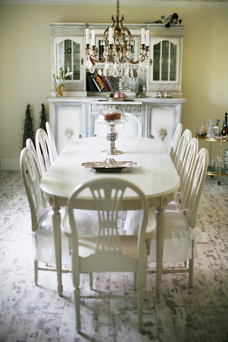 Essplatz in Weiß, Stühle mit Schonbezug auf Sitzflächen um ovalen Tisch, darüber mehrflammiger Kronleuchter