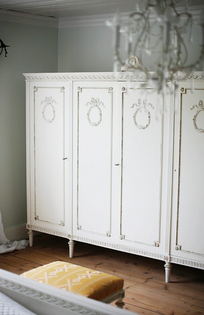 Elegant, antique cabinet on slim feet painted white and with carved doors in bedroom