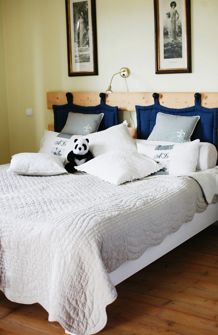 Double bed with quilt and blue quilted pads hanging from hooks on wooden headboard