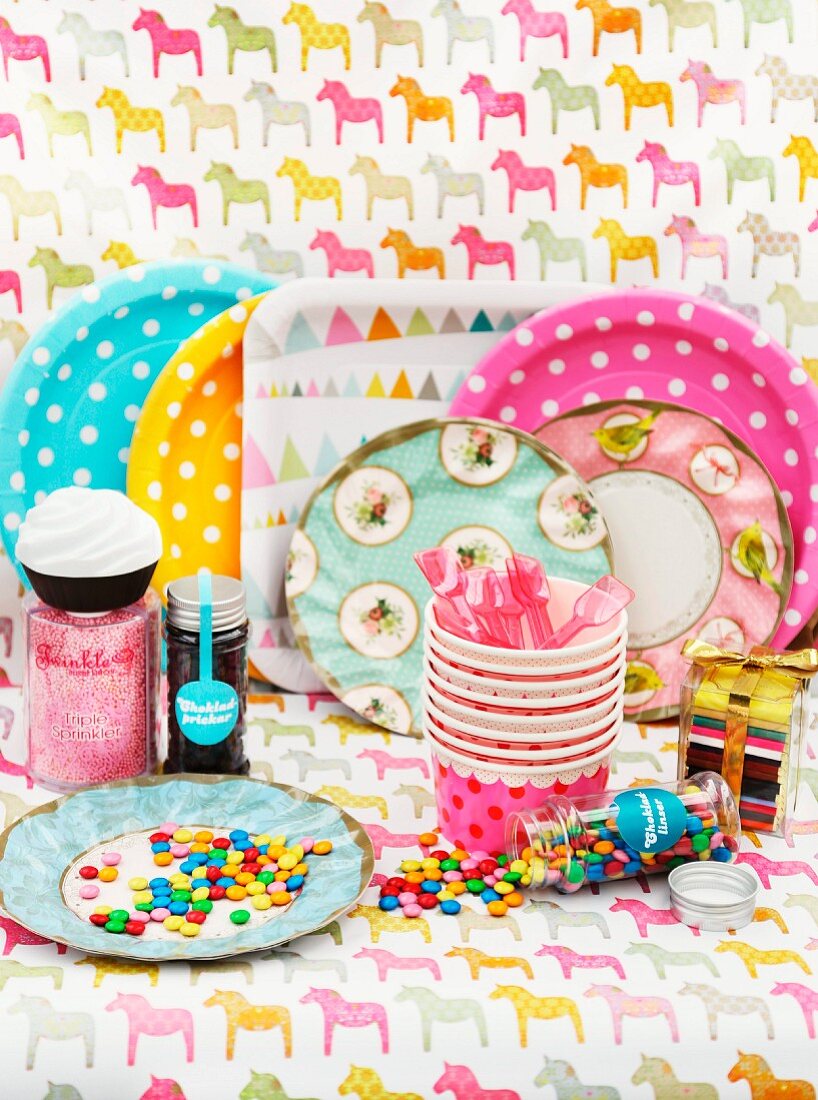 Colourful party tableware - paper plates, paper cups and colourful Smarties on decorative, horse-patterned paper