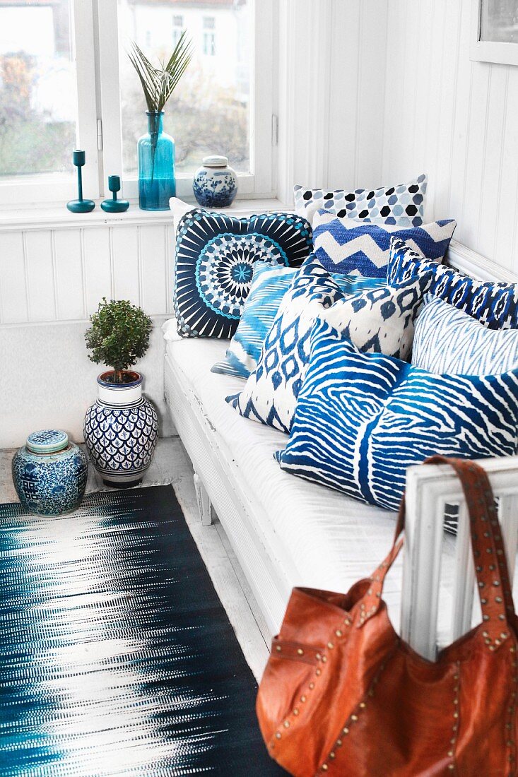 Weiß-blau gemusterte Kissen auf Sitzbank, in Zimmerecke vor weisser Holzverkleidung an Wand